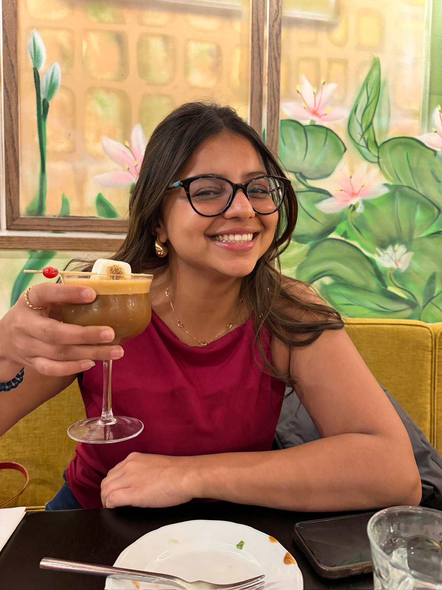 Kavya smiling in front of a painted lotus mural